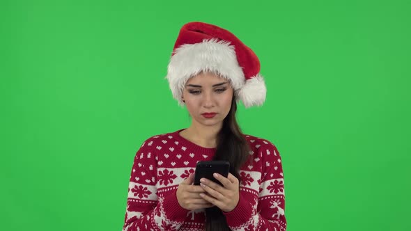 Portrait of Sweety Girl in Santa Claus Hat Is Texting on Her Phone. Green Screen