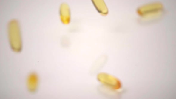 Slow Motion Macro of Yellow Pills Dropped onto White Background