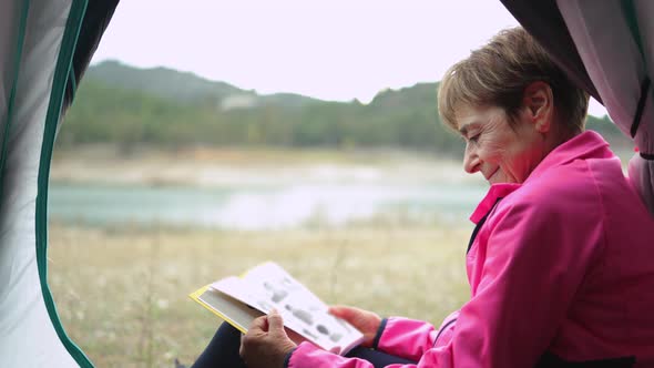 Senior Woman Inside Tent Reading a Book Camping Outdoor in Front of Lake Elderly People Travel in