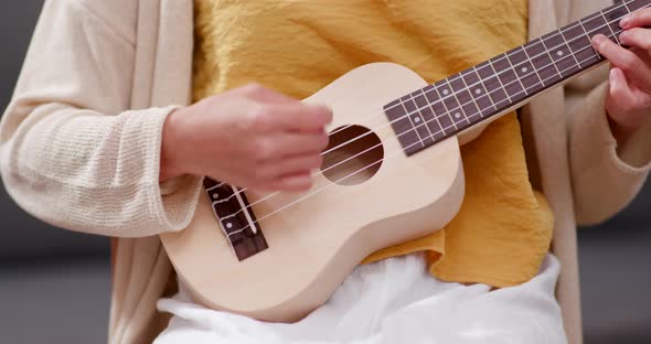 Woman practice ukulele and sitting on sofa at home