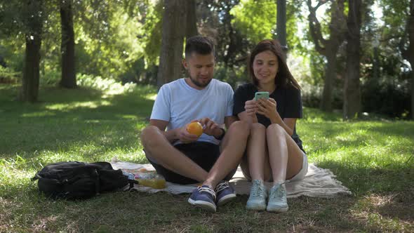 Happy Man and Woman Couple Using Tablet Pc and Mobile Phone They Sitting on the Grass Watching