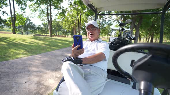 4K Asian senior businessman sitting on golf cart using mobile phone for corporate business working