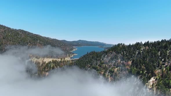 Drone flies over hills in fog towards Big Bear Lake, California, USA