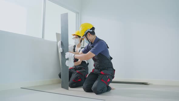 Asian builder worker people wear face mask installs laminate board on floor with constructuin team.