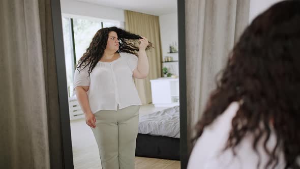 Young Overweight Woman Looks at Mirror with Disappointment