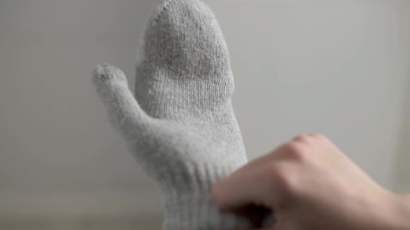 Girl puts on white knitted mittens on her hands.
