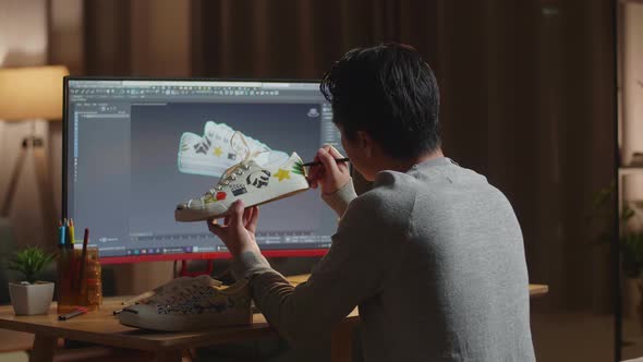 Male Footwear Designer Looking At A Desktop And Putting Coloured Unique Patterns On Sneakers At Home