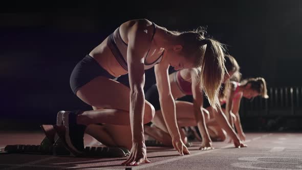 Side View of Three Women Preparing for a Run at the Stadium in the Dark in Slow Motion Starting and