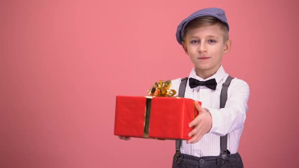 Boy Wearing Bow Tie and Suspenders Showing Gift Box to Camera, Holiday Present