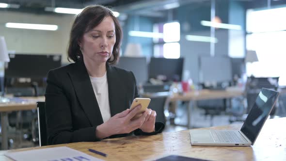 Cheerful Middle Aged Businesswoman Using Smartphone in Office