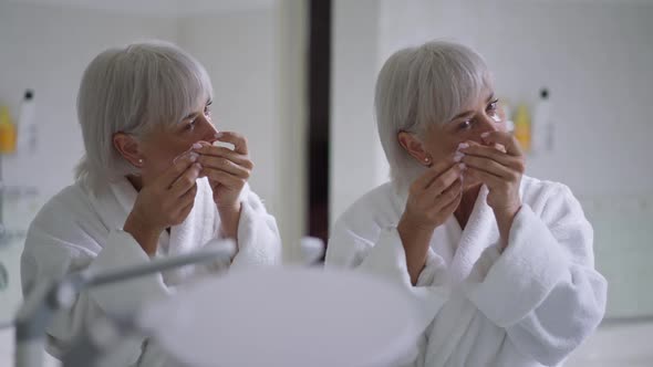 Reflection in Mirrors Senior Caucasian Woman Applying Eye Mask in the Morning at Home