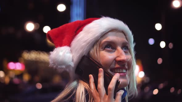 a woman chatting on her smartphone wearing a Santa hat is a night city.