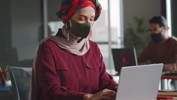 Female Office Worker in Hijab and Mask Working on Laptop