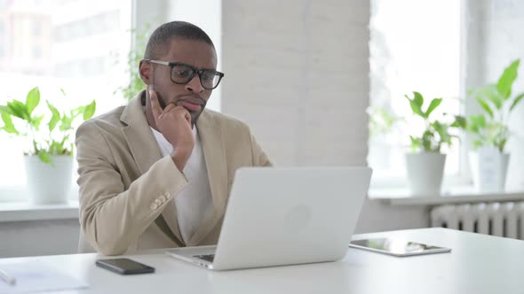 African Man Thinking While Working on Laptop in Office