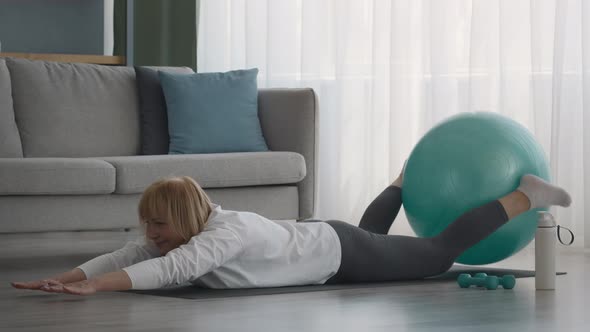 Senior Lady Exercising With Fitball Lying On Stomach At Home