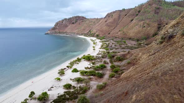 Aerial drone flyover a remote, secluded white sandy beach, coastal views and dry season hills in Dil
