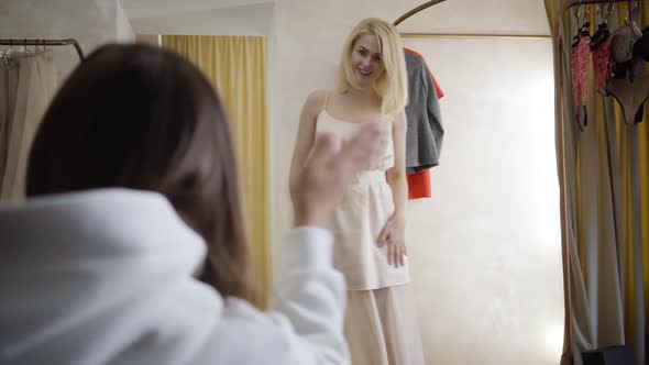 Portrait of Cheerful Young Blond Woman Spinning in New Elegant Beige Dress. Unrecognizable Friend