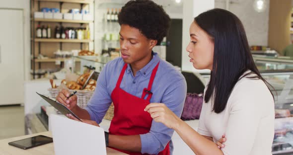 Video of diverse female owner and male waiter working with laptop at cafe shop