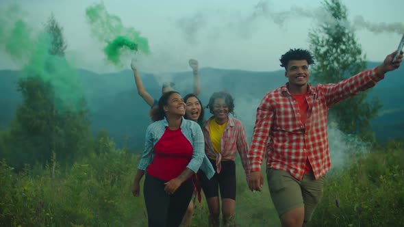 Carefree Diverse Multiethnic Friends with Colorful Smoke Bombs Walking Uphill at Sunset
