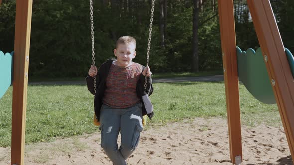 Caucasian Schoolage Boy Swings Relaxed on Swing Near Park Slow Motion