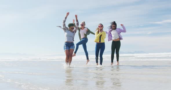 Happy group of diverse female friends having fun, dancing and smiling at the beach
