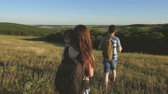 Travelers Go with Backpacks Through the Meadow. Family of Tourists with Children in the Countryside