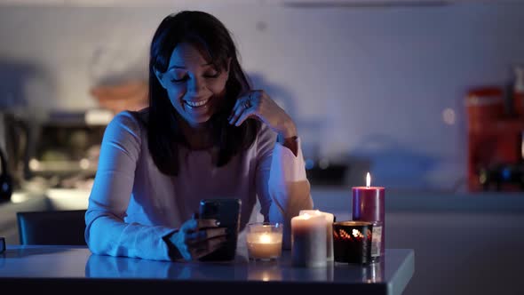 A Young Darkhaired Woman Is Sitting at a Table and Looking at a Smartphone Laughing in Front of Her