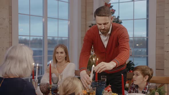 A Man Lights Candles at a Christmas Dinner Table with Family and Children