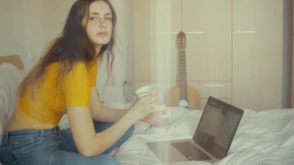 Woman with coffee and gadgets on bed