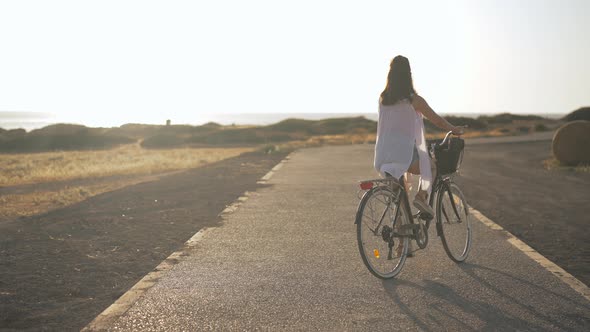 Back View Young Slim Woman Riding Bicycle in Slow Motion at Background of Cyprus Landscape at Sunset