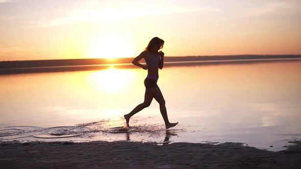 Silhouette of a Girl Running on the Water on a Sunset or Sunrise Background
