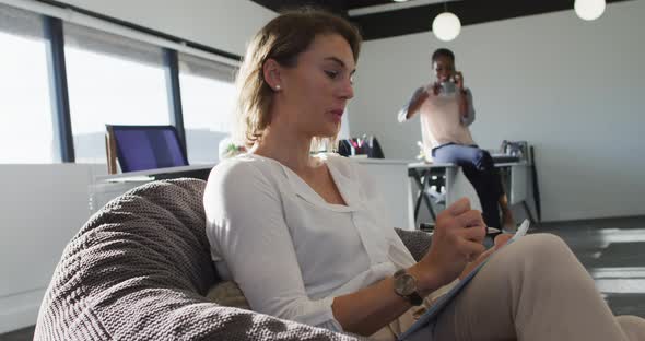 Caucasian businesswoman sitting in armchair, writing while her coworker having business call