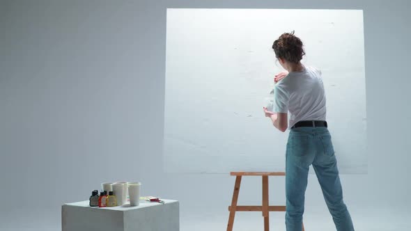 Back View Female Artist Applies a Layer of White Primer on a Large Canvas in a White Room a Talented