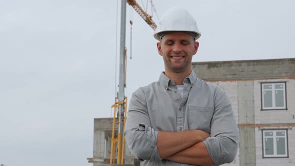 Architect in a Protective Builder's Helmet Against the Background of a House Under Construction