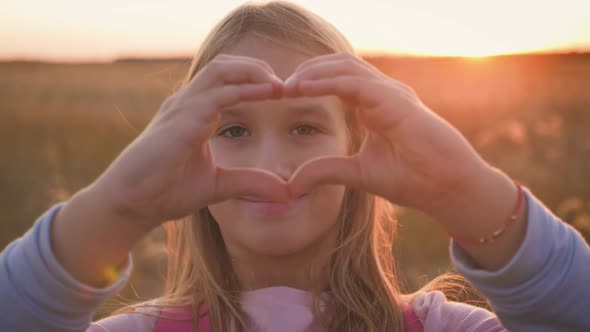 Little Girl Makes a Heart with Her Hands at Sunset.