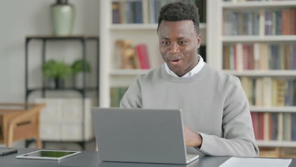 African Man Celebrating Success While Using Laptop in Library