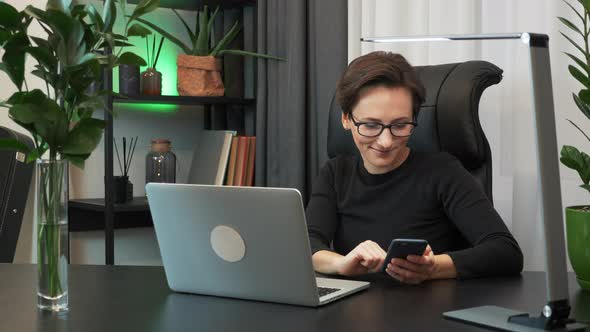 Woman is using smartphone sitting in modern office. Female works at workplace