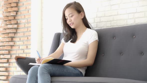 Beautiful young asian woman sitting on couch study and learning writing notebook at home.