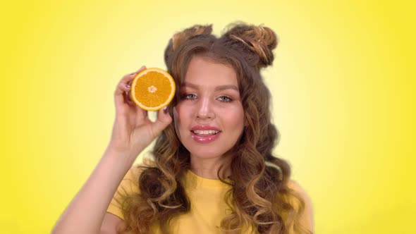 Beautiful Young Girl with Styling Poses with an Orange Winks and Smiles While Looking Into the