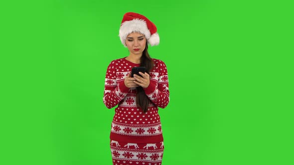 Sweety Girl in Santa Claus Hat Is Texting on Her Phone. Green Screen