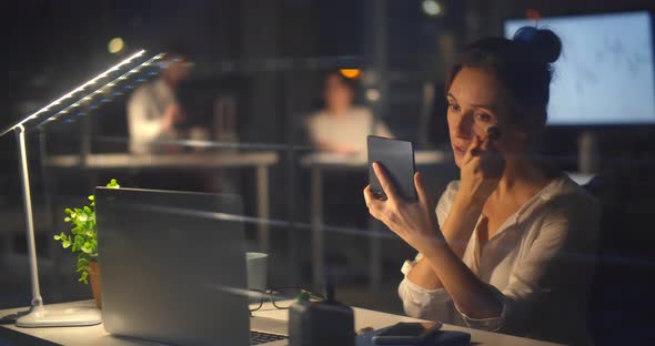 Young Businesswoman Doing Makeup at Workplace in Dark Office at Night