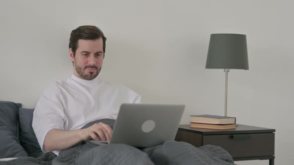 Young Man Working on Laptop in Bed