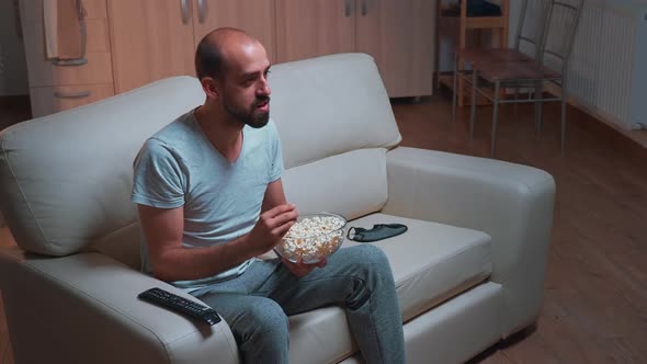 Caucasian Male Sitting on Couch with Popcorn Bowl in Hands While Looking at Movie Series