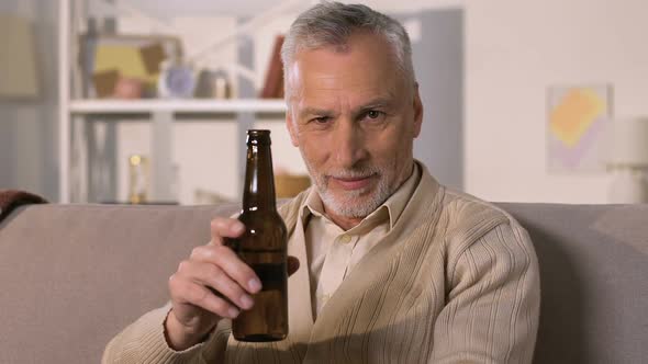 Handsome Aged Man Toasting in Camera and Drinking Beer Sitting on Sofa Closeup