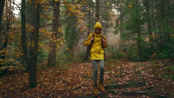 Slow Motion Pretty Woman in Yellow Jacket and Beany with Tourist Backpack Walking Through Wet Autumn
