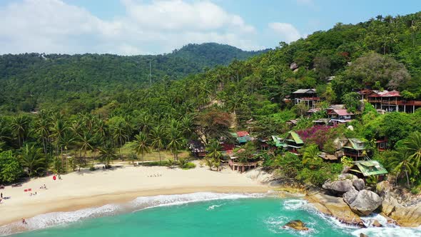 Elevated waterfront bungalows in the palm forest, foamy waves washing sandy beach on tropical Thaila