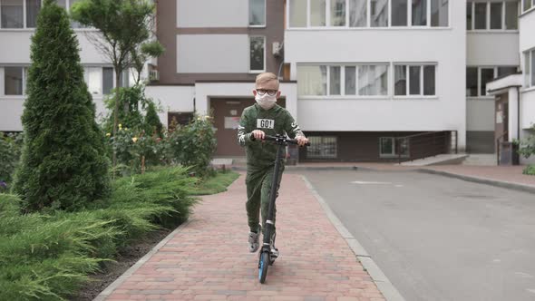 The boy rides a scooter during the quarantine period in a protective mask.