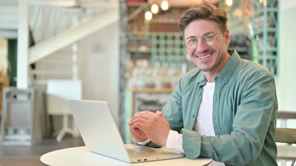 Middle Aged Man with Laptop Smiling at Camera in Cafe 