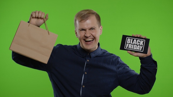 Man Showing Shopping Bags and Black Friday Inscription, Looking Astonished By Low Cost Purchase