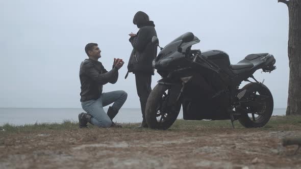 Wide Shot of Happy Boyfriend Proposing To Girlfriend on Cloudy River Bank Outdoors. Happy